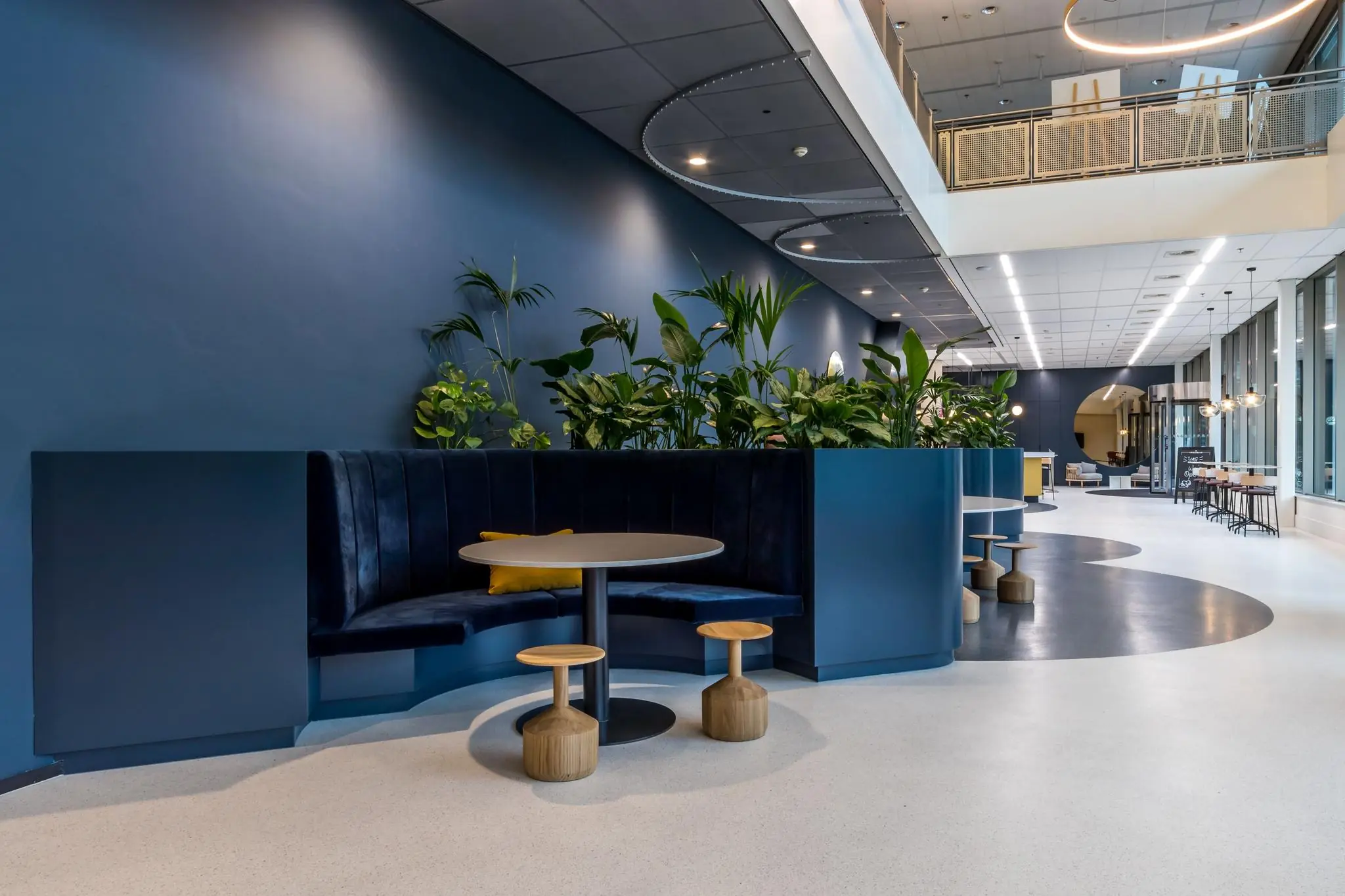 Moderne en open kantoorruimte aan de Vliegend Hertlaan met blauwe zitbanken, planten en ronde tafels.